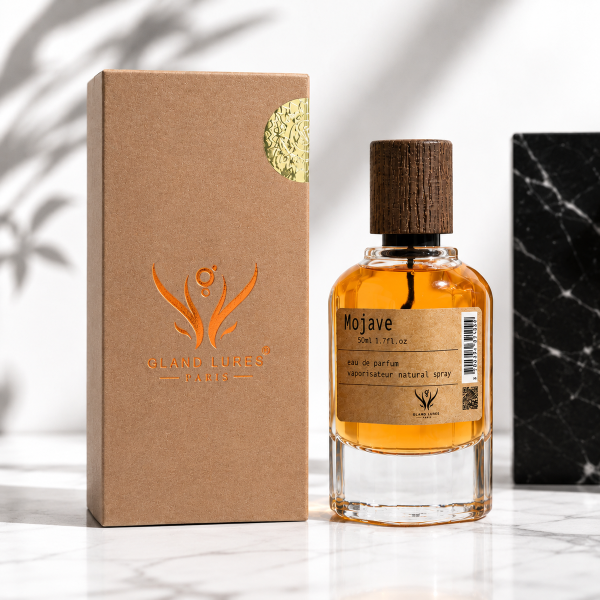 A bottle of Gland Lures Mojave natural spray perfume with amber liquid, a dark wood cap, and a brown paper label, standing next to its textured brown cardboard box on a white marble surface.