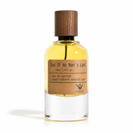 A 50ml glass bottle of 'Oud Of No Man's Land' natural perfume spray by Scenic Woods. The bottle is filled with a golden-yellow liquid and features a clear glass base, a brown wood-grain cap, and a brown kraft paper label.