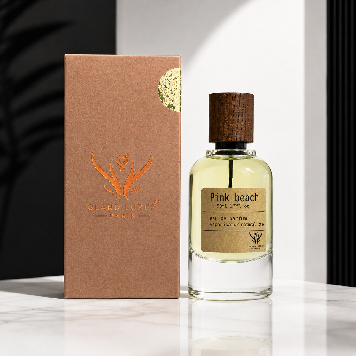 A clear glass perfume bottle labeled 'Pink beach' with pale yellow liquid and a dark wood cap, standing beside a brown kraft box with an orange logo on a white surface.