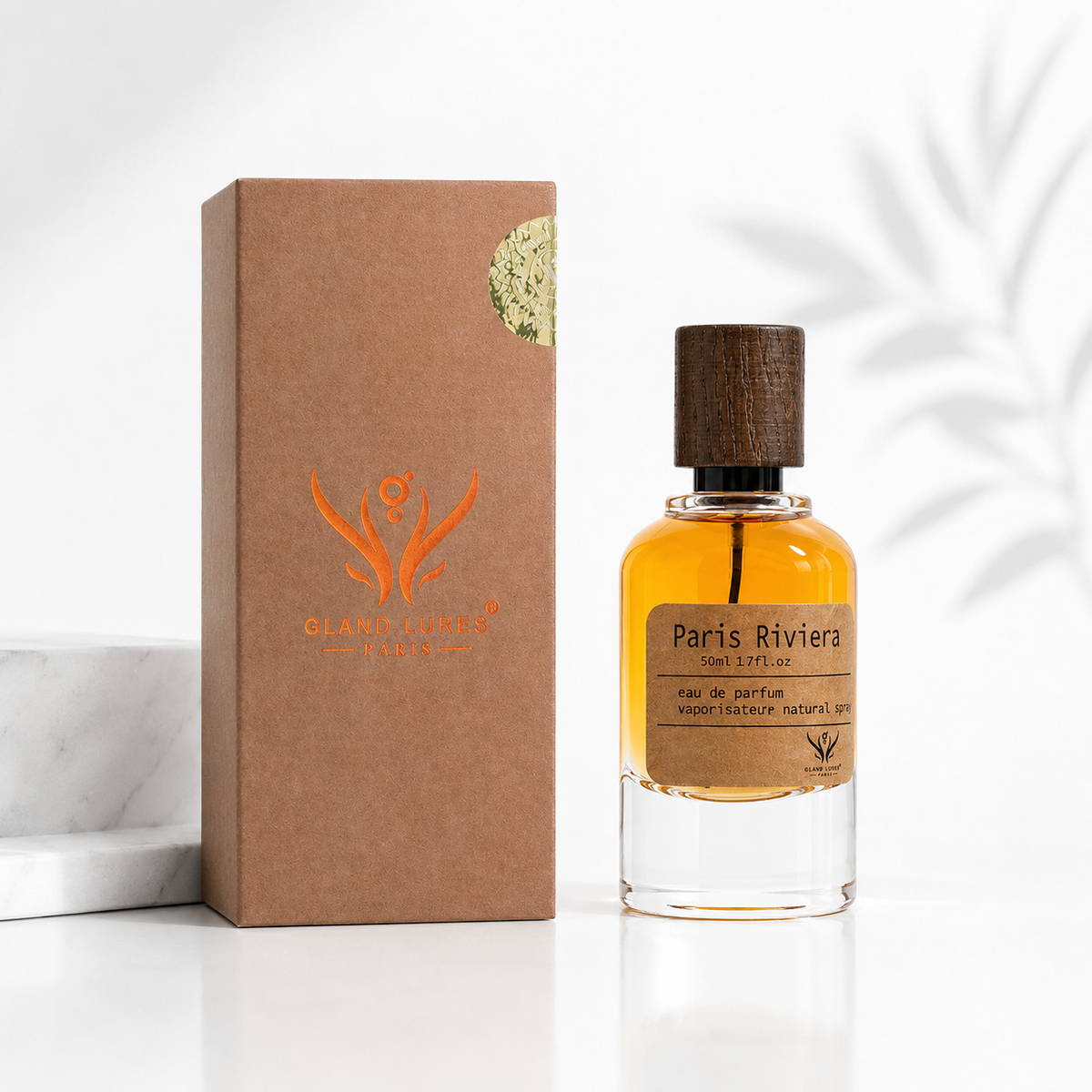 A bottle of Blanche & Lucie Paris Riviera Eau de Parfum with a clear glass body, amber liquid, and a dark wood cap, standing next to its brown kraft paper packaging box on a white surface.